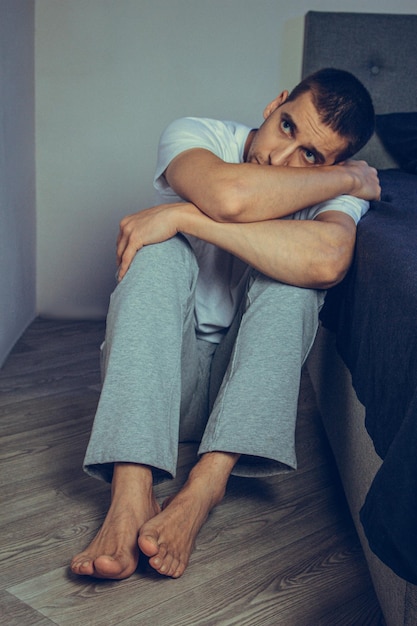 Dramatic lifestyle portrait of a handsome guy in his 30s and 40s sitting sadly on the bed feeling anxious and suffering from depression Attractive depressed and upset man in home bedroom