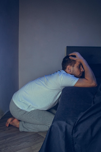 Dramatic lifestyle portrait of a handsome guy in his 30s and 40s sitting sadly on the bed feeling anxious and suffering from depression Attractive depressed and upset man in home bedroom