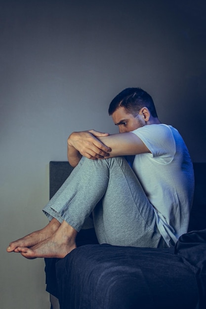 Dramatic lifestyle portrait of a handsome guy in his 30s and 40s sitting sadly on the bed feeling anxious and suffering from depression Attractive depressed and upset man in home bedroom