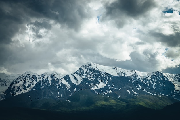 Dramatic mountains landscape with big snowy mountain ridge under cloudy sky. Dark atmospheric highland scenery with high mountain range in overcast weather. Awesome big mountains under gray clouds.