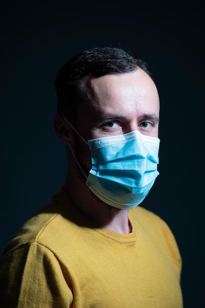 Dramatic portrait of a bearded guy in a protective medical mask and a yellow jacket. on a dark background.