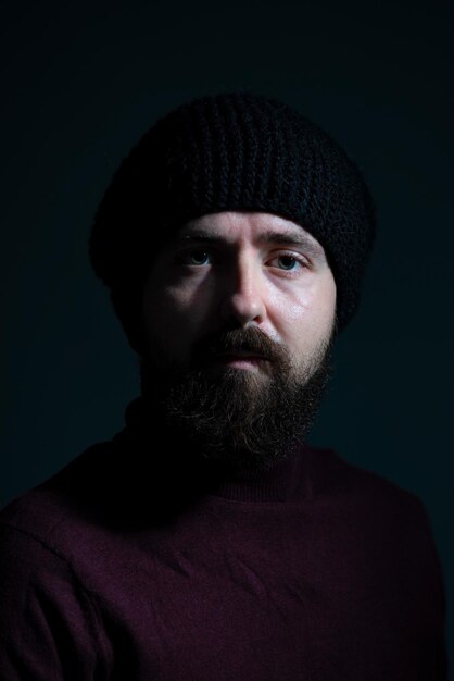Foto drammatico ritratto di millennial con cappello a maglia nero e maglione su sfondo scuro