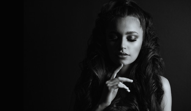 Dramatic portrait of a sensual young woman with curly hair posing in the shadows. Space for text