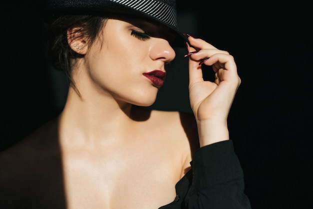 Ritratto drammatico della ragazza sexy in cappello nero con rossetto rosso