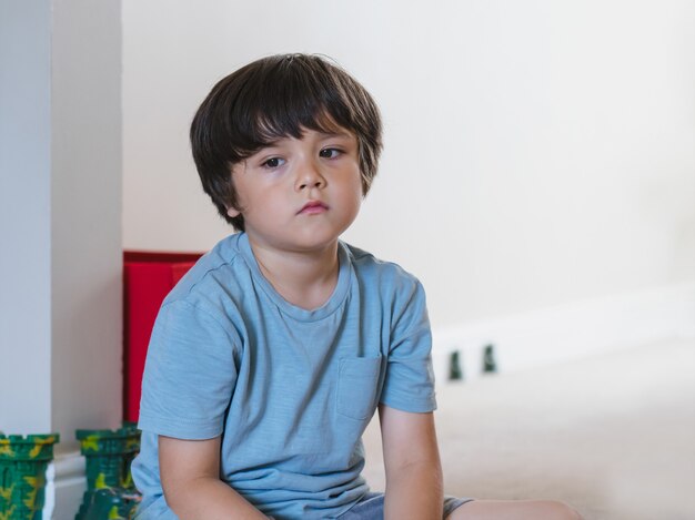 Dramatic portrait tired kid siting alone and looking out deep in thought