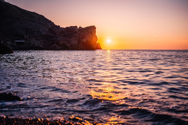 Drammatico paesaggio marino sulla spiaggia durante il tramonto con una scogliera rocciosa vulcanica illuminata dal caldo tramonto cielo sereno senza nuvole nessuno spazio di copia bellezza infinita della natura