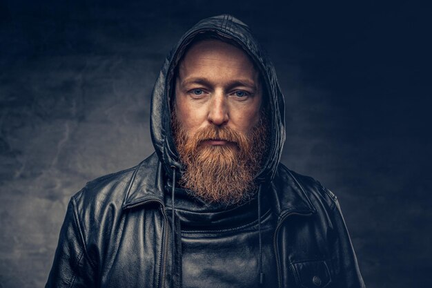 Dramatic studio portrait of redhead bearded male dressed in a leather jacket over dark grey vignette background.