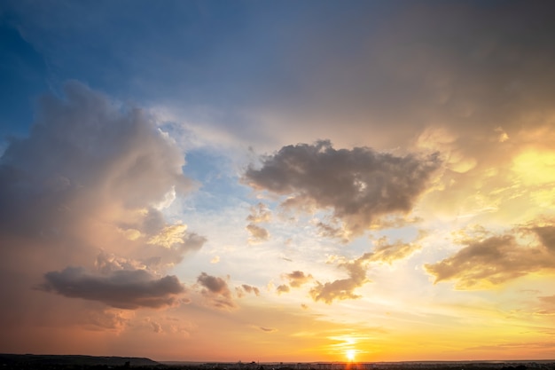 オレンジ色の夕日と青い空に照らされたふくらんでいる雲と農村地域の劇的な夕日の風景。