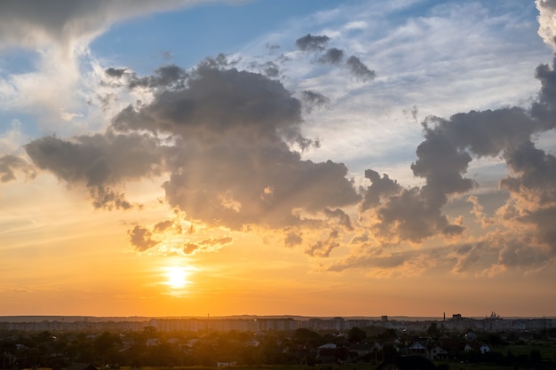 Dramatic sunset rural landscape with puffy clouds lit by orange setting sun and blue sky.