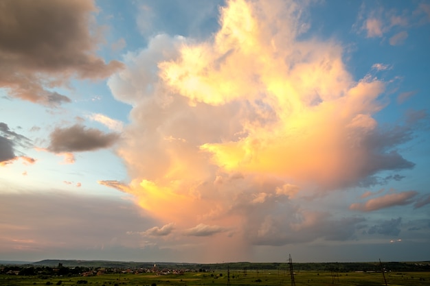 Dramatic yellow sunset over rural area with stormy puffy clouds lit by orange setting sun and blue sky.