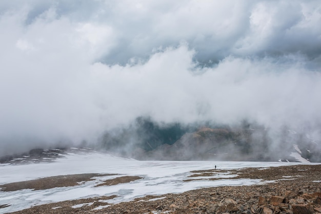 Dramatisch landschap met mensen in een wolk boven een bonte bergvallei Toeristen in een wolk boven een veelkleurige vallei Lage wolk op stenen heuvel met sneeuw Geweldig hoog berglandschap in lage wolken
