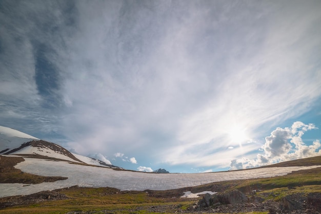 Dramatisch landschap met zonovergoten besneeuwde bergkam tegen spitse top met sneeuw in zonlicht in bewolkte lucht bij veranderlijk weer kleurrijk zonnig landschap met gletsjer en besneeuwde bergtop