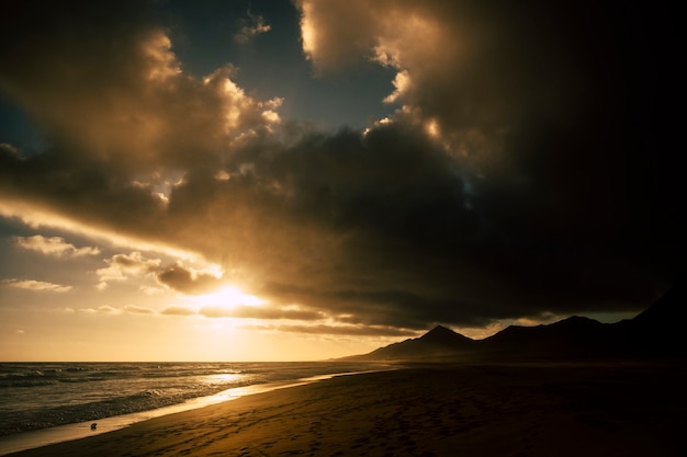Dramatische donkere schaduwen zonsondergang op het strand met zwarte bergen op de achtergrond - zon en oceaan voor avontuur concept - schilderachtig landschap en mooie lucht met wolken