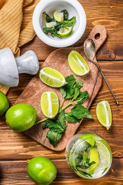 Drank maken van gereedschappen en ingrediënten voor cocktail, limonade, mojito. Limoen, ijs en munt. Houten achtergrond. Bovenaanzicht.