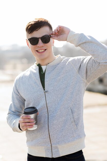 dranken en mensen concept - glimlachende jonge man of tiener die koffie drinkt uit een papieren beker buitenshuis