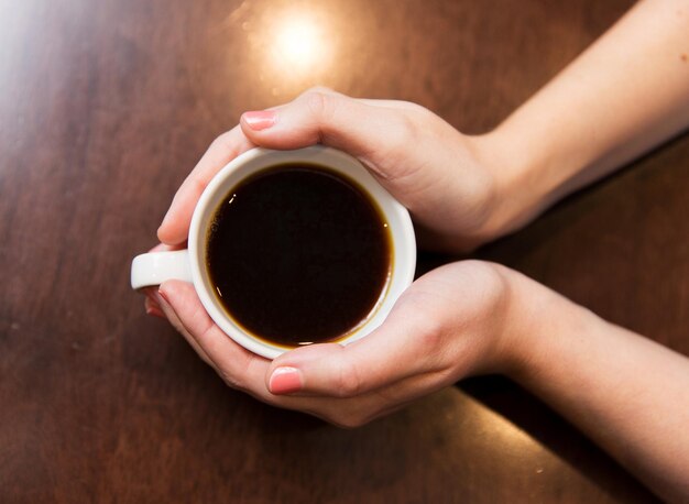 dranken, mensen en levensstijlconcept - close-up van vrouwenhanden met beker met hete zwarte koffie