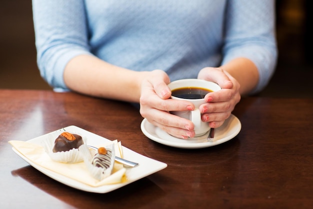 dranken, mensen en levensstijlconcept - close-up van vrouwenhanden met kop met hete zwarte koffie en dessert