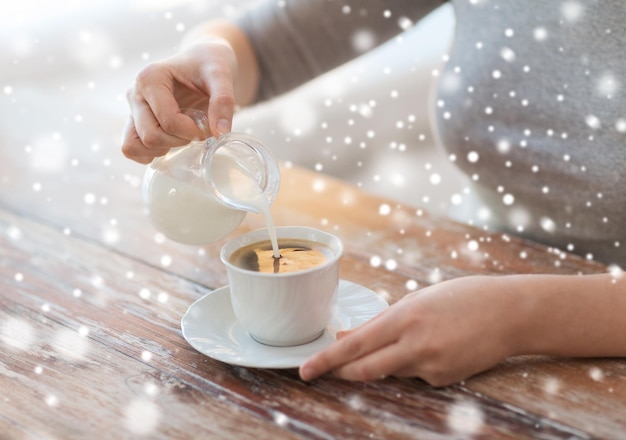 drankjes, mensen en thuisconcept - close-up van een vrouw die aan tafel zit en melk in een koffiekopje giet