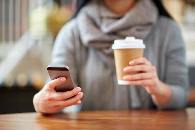 drankjes, mensen, technologie en lifestyle concept - close-up van vrouw met smartphone en koffie in café