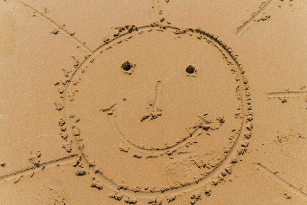 Il disegno sulla sabbia della spiaggia raffigura un sole stilizzato con un sorriso e gli occhi