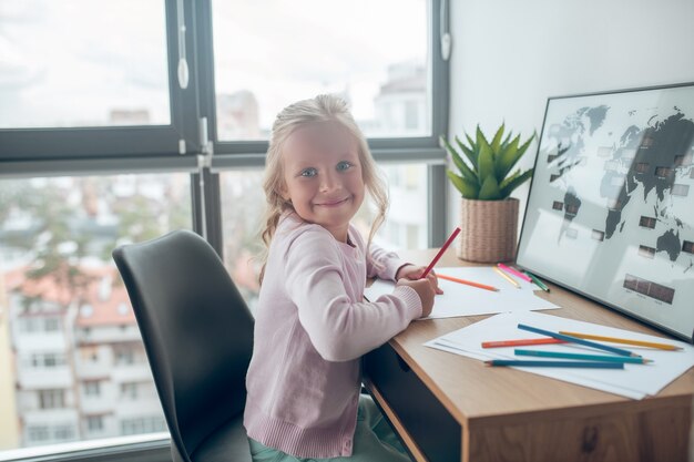 Drawing. A cute blonde girl sitting at the table and smiling