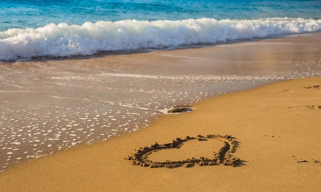 Drawing a heart on the beach sand near sea waves