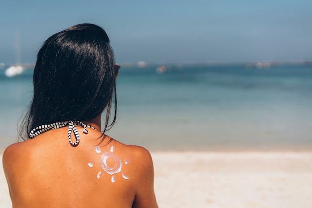 Photo drawing of a sun with sun protection cream in the shoulder of a tanned woman in the beach.