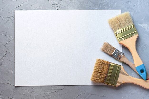 Drawing tools paintbrushes with blank white paper sheet background, top view