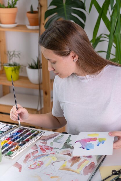 Drawing in watercolor on a white sheet A young woman paints in watercolor at home on a white sheet