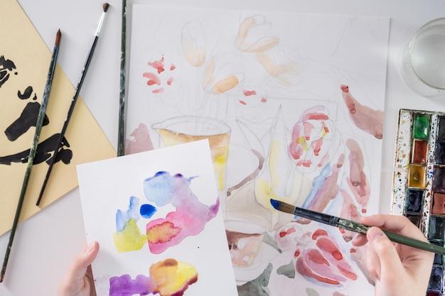 Drawing in watercolor on a white sheet A young woman paints in watercolor at home on a white sheet