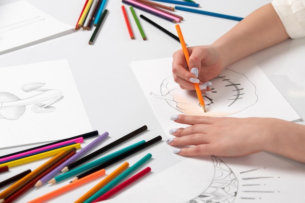 Drawing a young girl hand drawing a halloween pumpkin with orange pencil behind the table