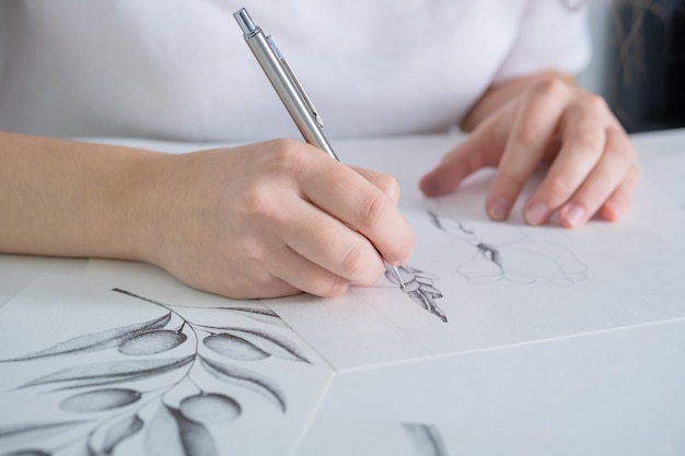 Drawings made in pencil are on the table a young woman of\
european appearance draws with a pencil on white paper graphics the\
process of drawing with a pencil at home at a white table