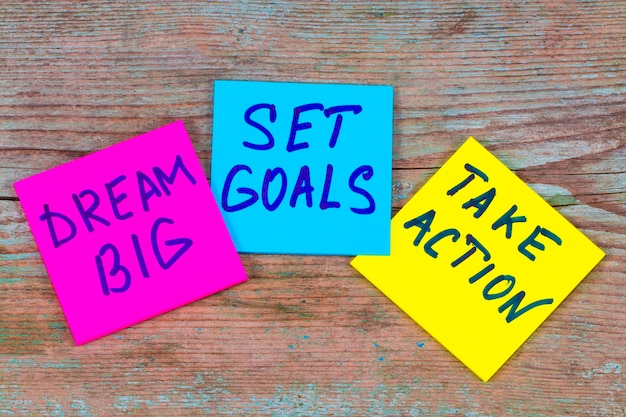 Photo dream big, set goals, take action concept - motivational advice or reminder on colorful sticky notes on wooden background.