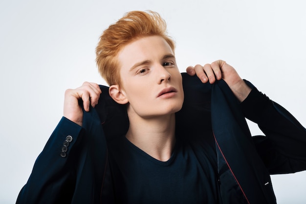 Dreamboat. good-looking humourless red-haired young man putting his jacket on and staring and having a modern haircut