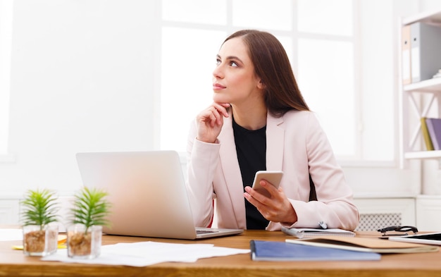 Dreaming about vacation. Relaxed business woman sitting at workplace with smartphone in modern office, copy space