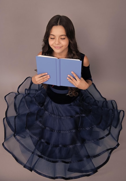 드레스를 입은 꿈꾸는 여학생은 책과 카피북을 배울 준비가 되어 있습니다. 학교 아이들은 고립된 회색 배경에서 꿈을 꿉니다