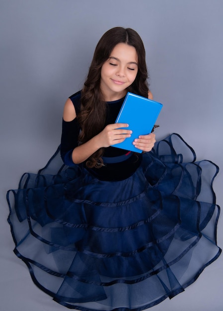 夢を見てドレスを着た女子高生は本とコピーブックを学ぶ準備ができて孤立した灰色の背景に学校の子供たちを驚かせた