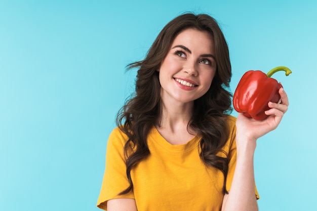 dreaming smiling young beautiful woman posing isolated over blue wall holding paprika.