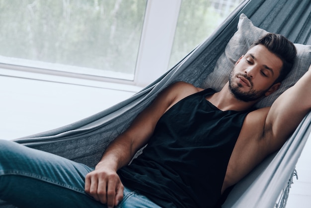 Dreaming. Top view of handsome young man in casual clothing sleeping while lying in the hammock indoors