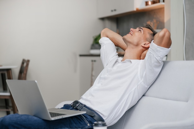 Dreaming young man with a laptop sitting on couch