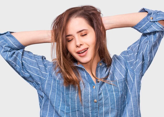 Dreaming young woman dressed casual striped blue shirt wake up in the morning Positive girl posing against white studio backround People emotions
