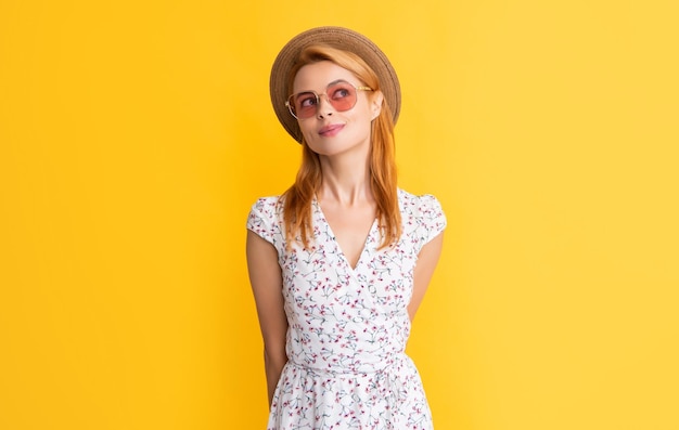 Dreaming young woman in straw hat and sunglasses on yellow background
