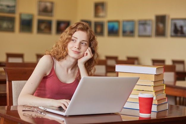 dreamy adorable young lady looking aside, sitting at table in reading hall