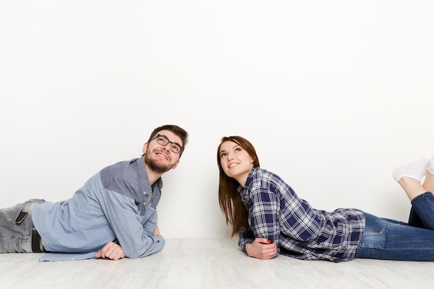 Foto coppia sognante sdraiata sul pavimento in una stanza vuota e guardando in alto, immagina un futuro progetto di interior design, sfondo bianco