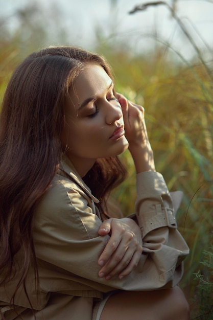 Dreamy gentle woman in a beige raincoat in nature Romantic young woman in thick tall grass in field Natural beauty enjoyment of life