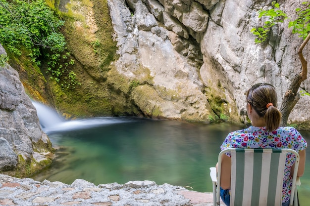 Мечтательная девушка медитирует в зеленой лагуне возле водопада