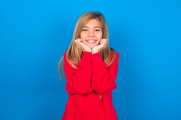 Dreamy girl keeps hands pressed together under chin looks with happy expression has toothy smile