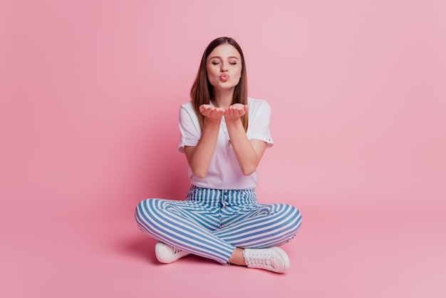 Dreamy inspired young lady hold palms send air kisses over pink background