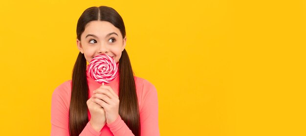 Ragazzo sognante con caramella lecca-lecca su bastone su sfondo giallo caramello bambino adolescente con lo spazio della copia dell'intestazione del banner del poster dei dolci