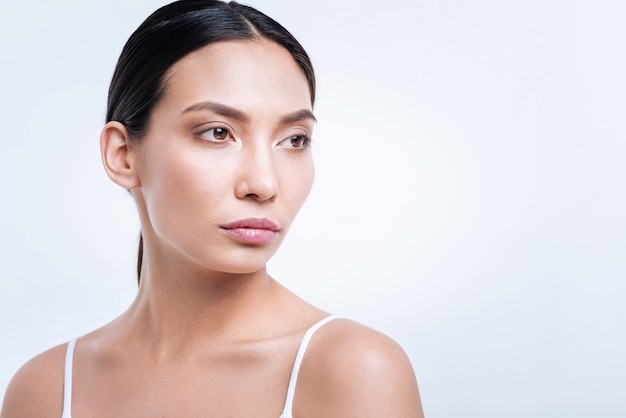 Dreamy look. The portrait of a pretty dark-haired woman with a pony tail looking into the distance while posing